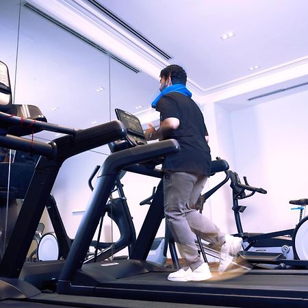 מכה Makarem Ajyad Makkah Hotel מראה חיצוני תמונה The photo shows a person exercising on a treadmill in a modern gym or fitness room. The individual is wearing a blue neck support while jogging on the treadmill, which is set against a backdrop of large mirrors. There are also additional exercise equ