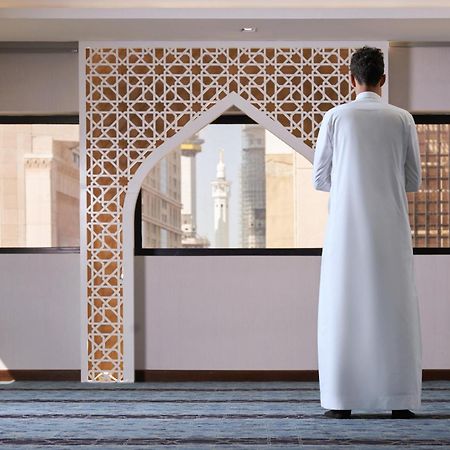 מכה Makarem Ajyad Makkah Hotel מראה חיצוני תמונה The photo depicts a person standing with their back facing the viewer, wearing a traditional white garment. They are in a spacious interior setting that features an ornate archway with intricate patterns, typical of Islamic architecture. Through the 