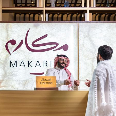 מכה Makarem Ajyad Makkah Hotel מראה חיצוני תמונה The photo depicts a reception area in a hotel or establishment named "Makarem." In the image, a receptionist, dressed in traditional attire, is smiling and interacting with a guest who is wearing a white robe, commonly known as a thobe or ihram. The 