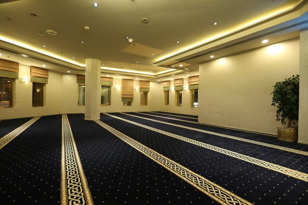מכה Makarem Ajyad Makkah Hotel מראה חיצוני תמונה The photo shows a spacious indoor area with a plush blue carpet featuring a decorative pattern. The room is well-lit, with soft lighting along the ceiling. There are several windows, allowing natural light to enter, and a few plants are positioned ar
