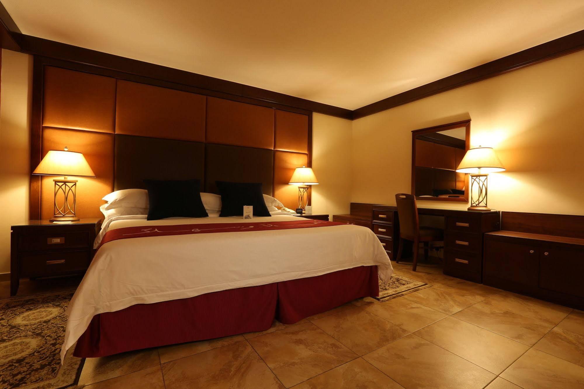 מכה Makarem Ajyad Makkah Hotel מראה חיצוני תמונה The photo shows a well-appointed hotel room with a cozy and inviting atmosphere. It features a large bed with a white comforter and dark pillows, positioned against a wooden headboard. There are two bedside lamps providing soft lighting on either sid