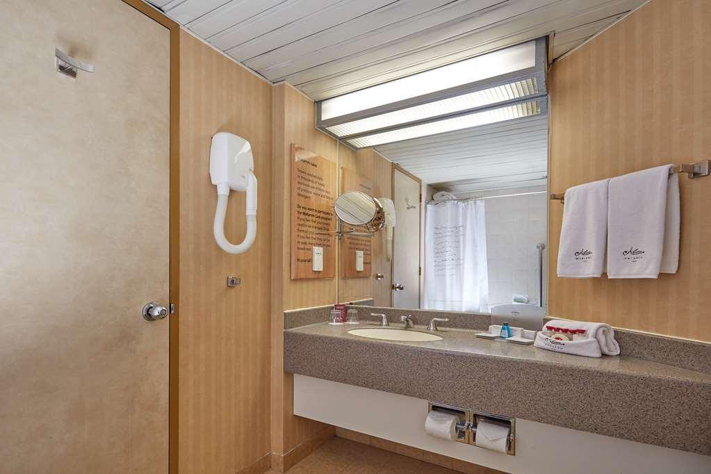 מכה Makarem Ajyad Makkah Hotel מראה חיצוני תמונה The photo shows the interior of a bathroom. It features a light-colored wall with vertical stripes and a ceiling that is white and textured. There is a gray countertop with a sink and a mirror above it. On one side, there are two white towels hanging