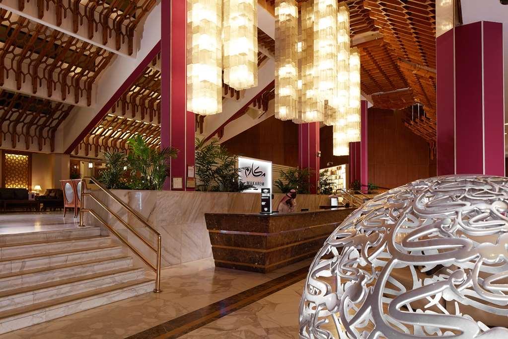 מכה Makarem Ajyad Makkah Hotel מראה פנימי תמונה The photo depicts a luxurious hotel lobby. It features a grand entrance with a staircase leading up to a reception area. The lobby has high ceilings adorned with striking, modern light fixtures that hang down, providing a warm ambiance. The walls are