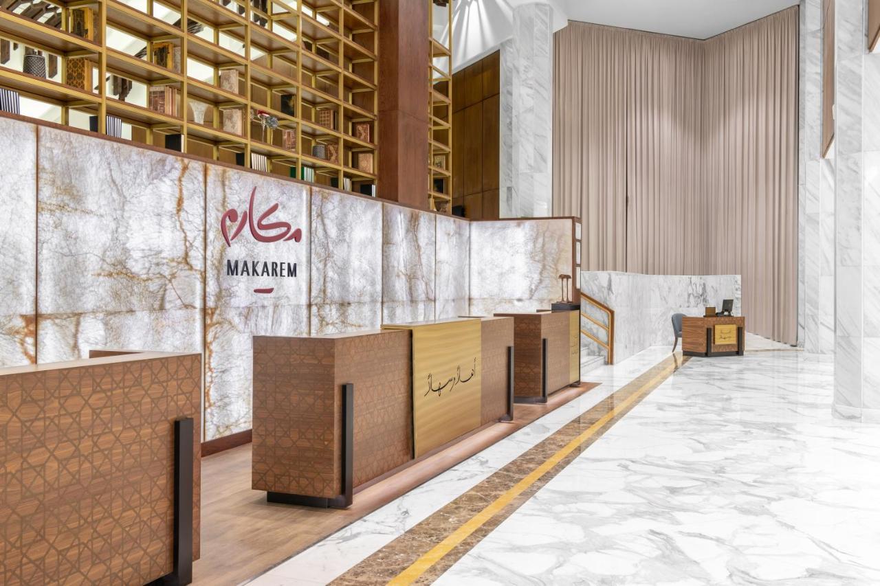 מכה Makarem Ajyad Makkah Hotel מראה חיצוני תמונה The photo shows a modern hotel reception area with a sleek design. The reception desk is made of a combination of wood and stone, featuring a warm color palette. The backdrop is adorned with a marble finish, giving a luxurious feel. Above the desk, t