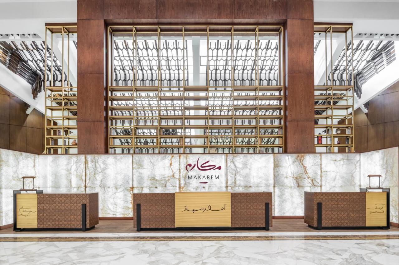 מכה Makarem Ajyad Makkah Hotel מראה חיצוני תמונה The photo shows the interior of a hotel or a reception area, characterized by a modern and elegant design. In the foreground, there are multiple reception desks with a polished finish. Behind the desks, a striking feature is a wooden wall with a geom