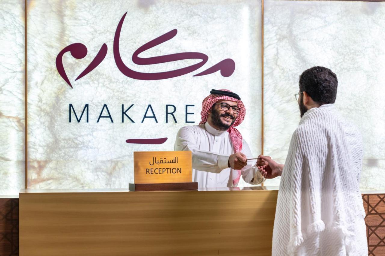 מכה Makarem Ajyad Makkah Hotel מראה חיצוני תמונה The photo shows a reception area with a sign that reads "MAKARE" in both Arabic and English. In the foreground, a staff member wearing traditional attire is smiling and shaking hands with a visitor, who is clad in a white garment, typical for formal 