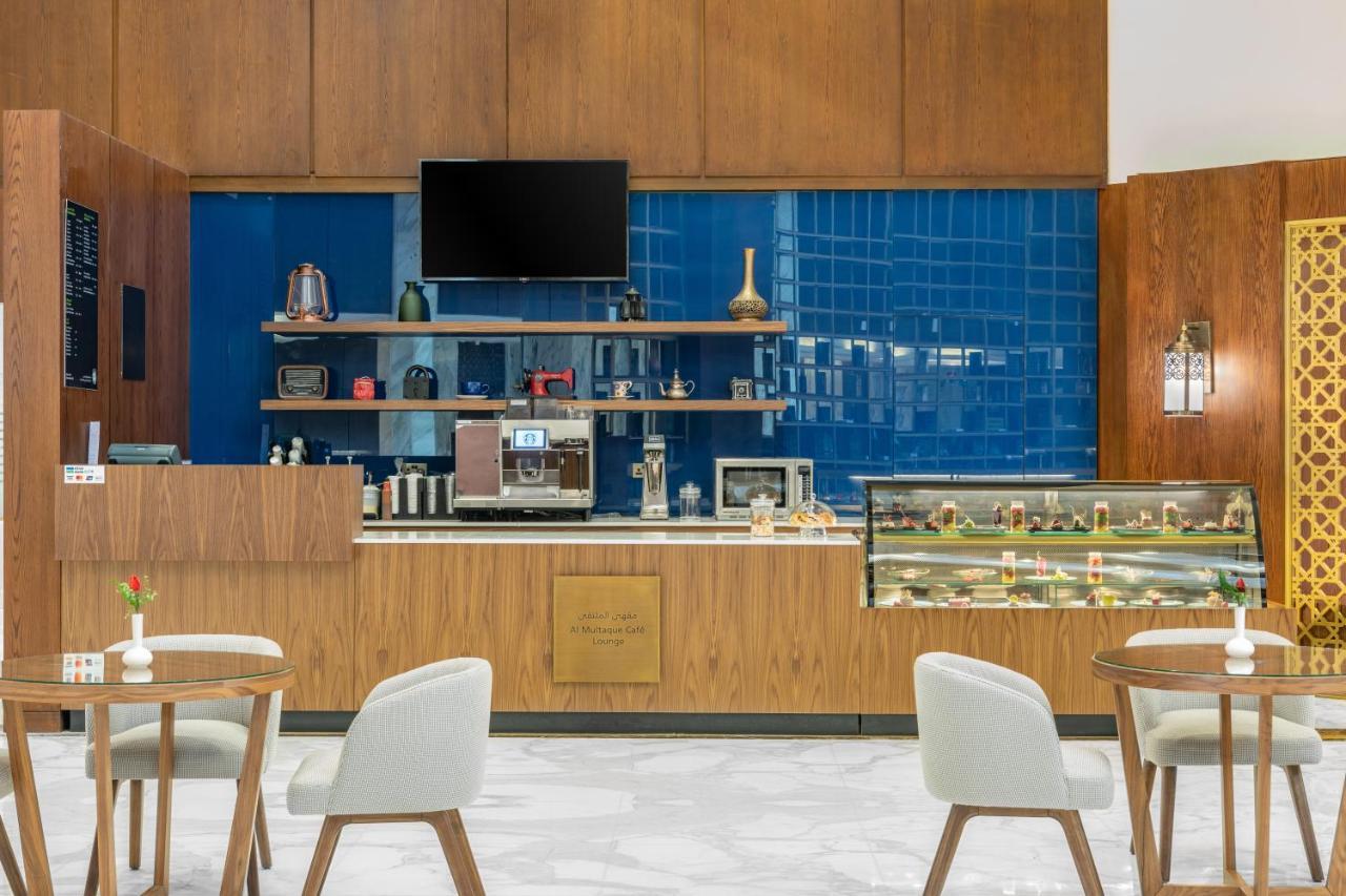 מכה Makarem Ajyad Makkah Hotel מראה חיצוני תמונה The photo shows the interior of a café. The design features warm wood paneling and a striking blue tiled wall. In the foreground, there are several light-colored chairs and small tables arranged neatly. Behind the counter, there's a variety of coffee