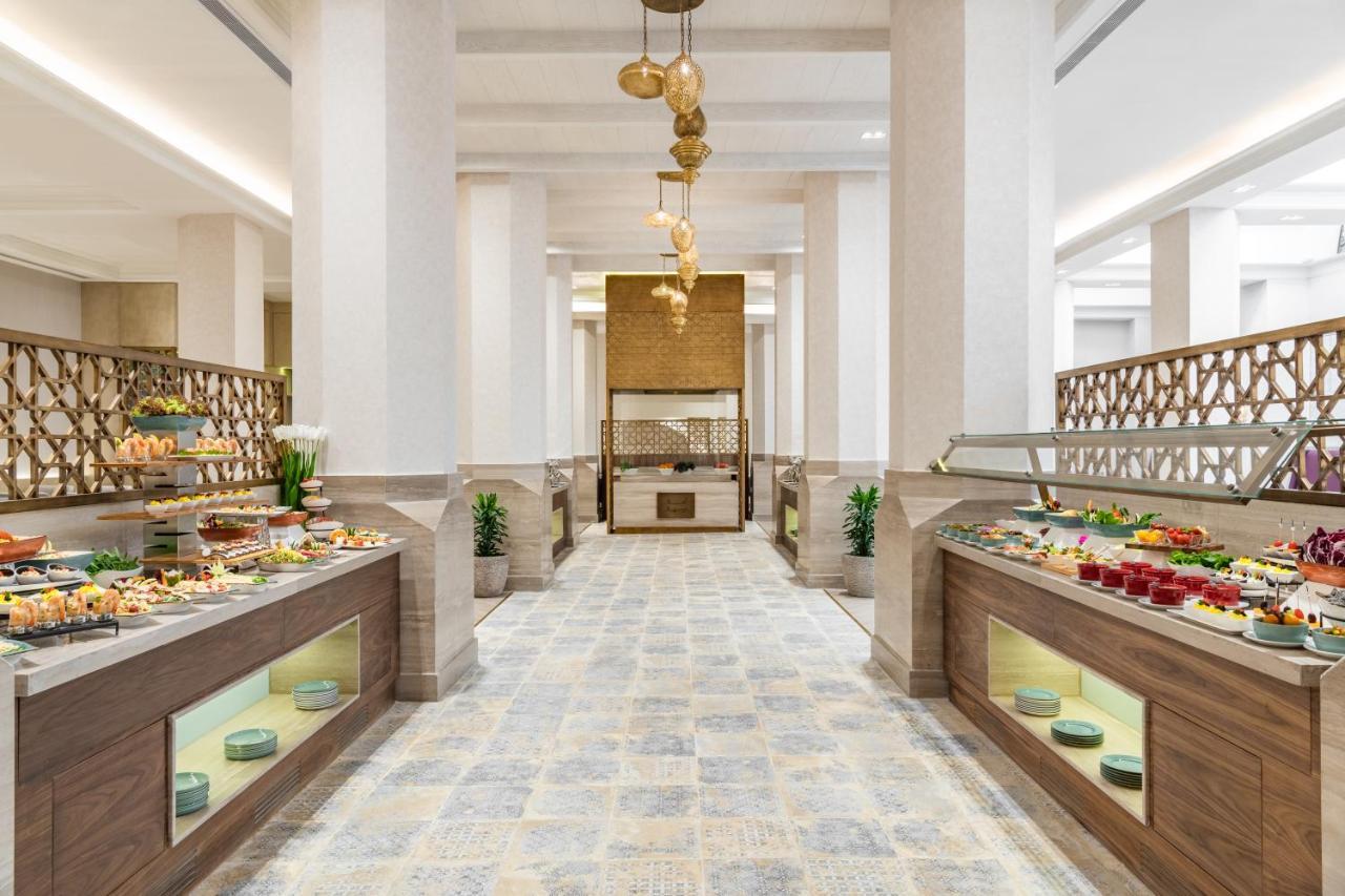 מכה Makarem Ajyad Makkah Hotel מראה חיצוני תמונה The photo shows an elegant restaurant or buffet area. There are two long buffet tables on either side, displaying a variety of colorful dishes and desserts. The tables have an organized layout and are adorned with small plants. In the center of the r
