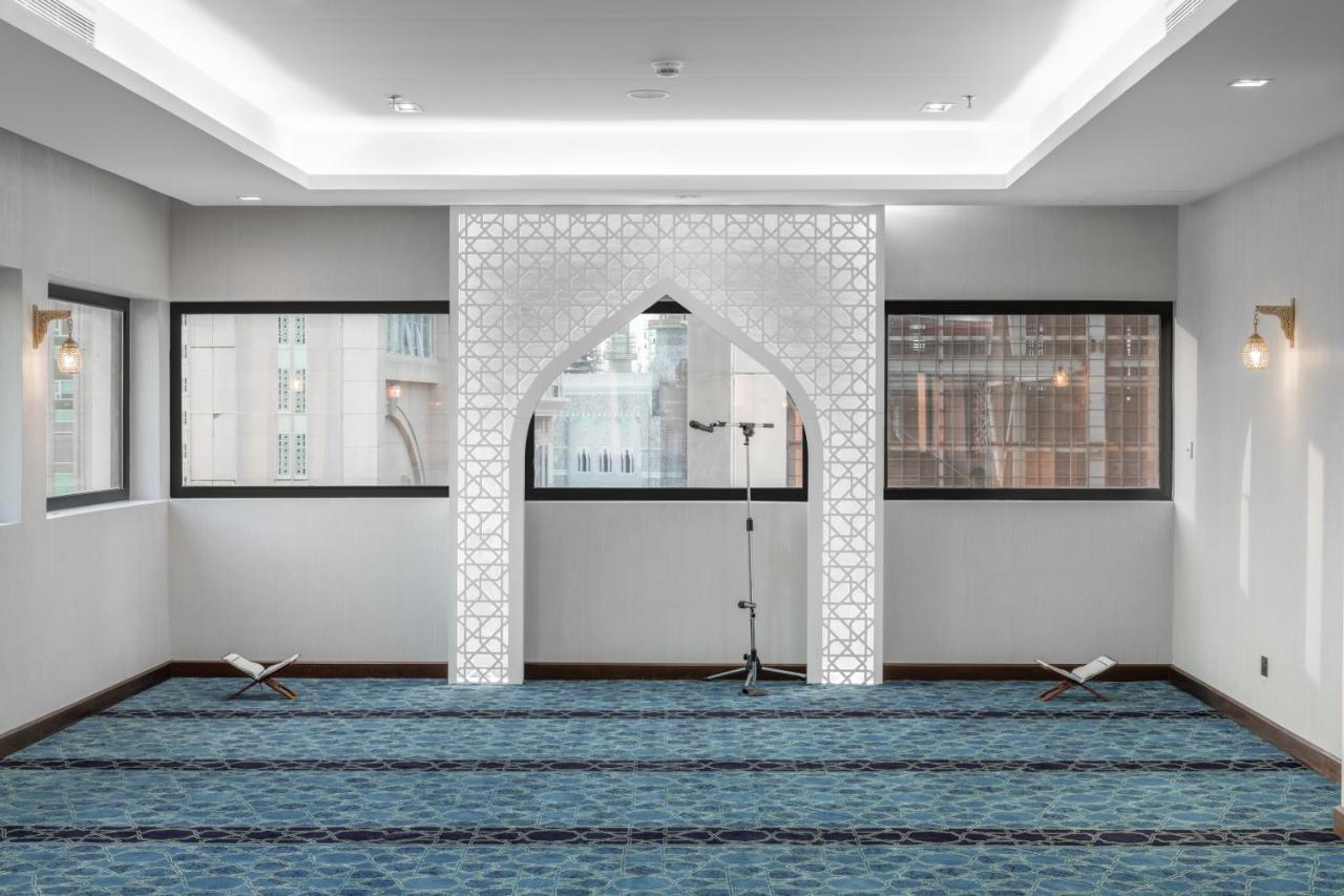 מכה Makarem Ajyad Makkah Hotel מראה חיצוני תמונה The image shows a prayer room or small mosque interior. It features a white decorative wall with an archway that is typical in Islamic architecture. The floor is covered with a blue carpet, arranged with patterned lines, likely indicating prayer spot