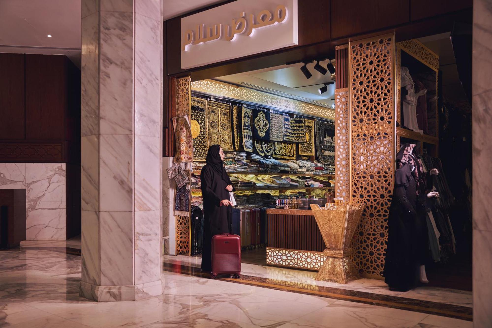 מכה Makarem Ajyad Makkah Hotel מראה חיצוני תמונה The photo shows a storefront that appears to sell traditional textiles or garments. The entrance features intricate decorative patterns, typical of Middle Eastern architecture. A woman is standing outside the shop, dressed in a black abaya, and she h