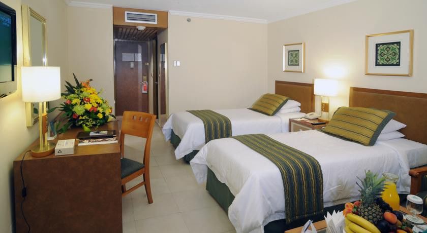 מכה Makarem Ajyad Makkah Hotel מראה חיצוני תמונה The photo shows an interior of a hotel room featuring two twin beds with white linens and green decorative accents. The walls are painted in a light beige color, and there is a small table next to one of the beds. A desk with a chair is positioned ne