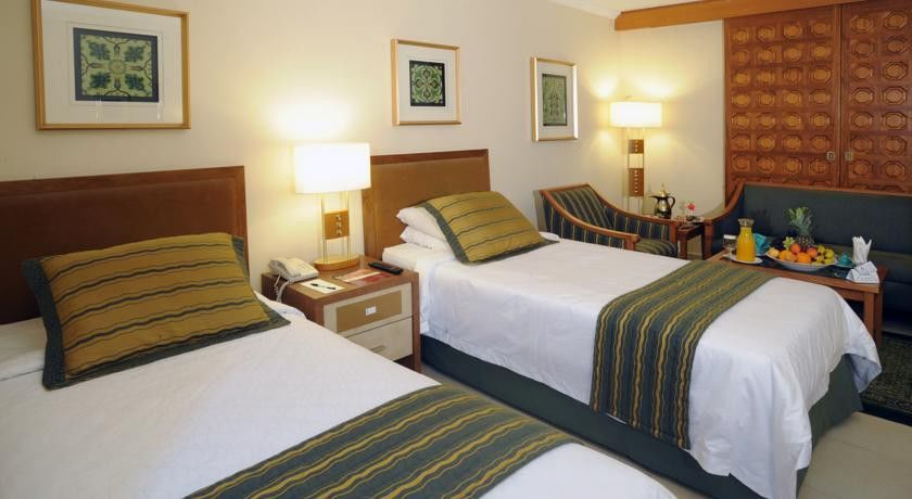 מכה Makarem Ajyad Makkah Hotel מראה חיצוני תמונה The photo shows a hotel room with two twin beds, each topped with decorative green and gold striped bed runners. There is a nightstand between the beds with a lamp on it. The room features light-colored walls, framed artwork on the walls, and a small